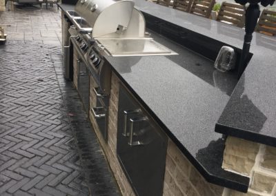Yellow Brick Outdoor Kitchen with Black Countertops, and Grill