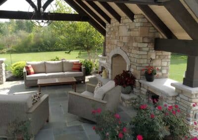 Comfortable furniture and a statement chandelier create a cozy seating area around the outdoor fireplace that is seamlessly integrated into the overhead structure.