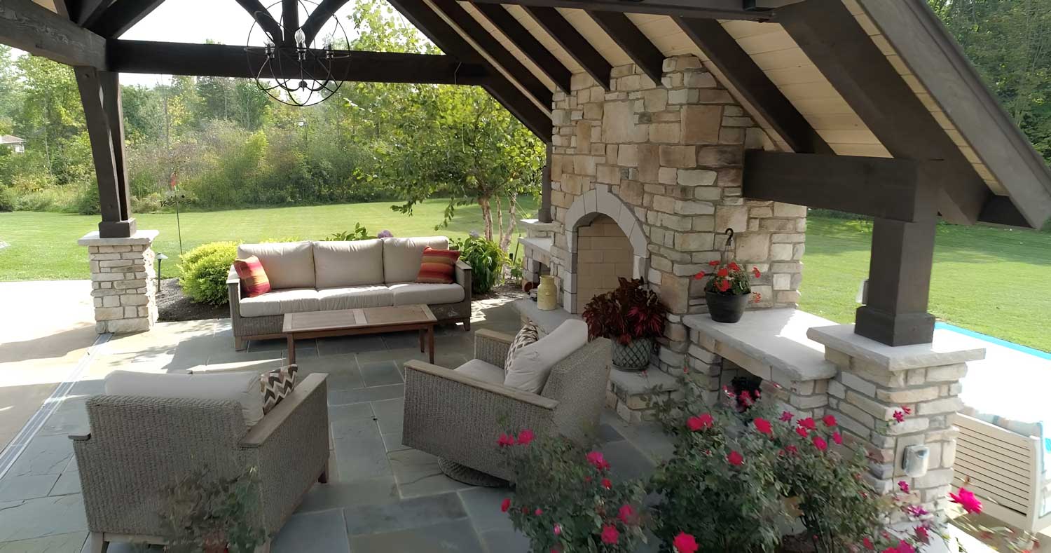 Comfortable furniture and a statement chandelier create a cozy seating area around the outdoor fireplace that is seamlessly integrated into the overhead structure.