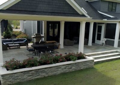 A covered porch offers cozy outdoor seating and dining areas in a quiet space away from the action of the pool. Custom planters and additional landscaping add color and texture.