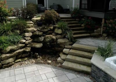 Brothers Grimm landscaping design includes a natural-looking water feature, rugged rocks and lush plantings that soften the border between house and pool.