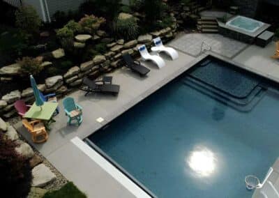 The contemporary poured concrete hardscape around the pool provides ample space for a variety of seating areas, including lounge chairs for sunbathing.