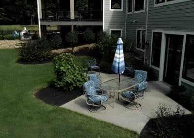 The side patio allows easy access from the home to an outdoor dining area surrounded by flowering bushes.