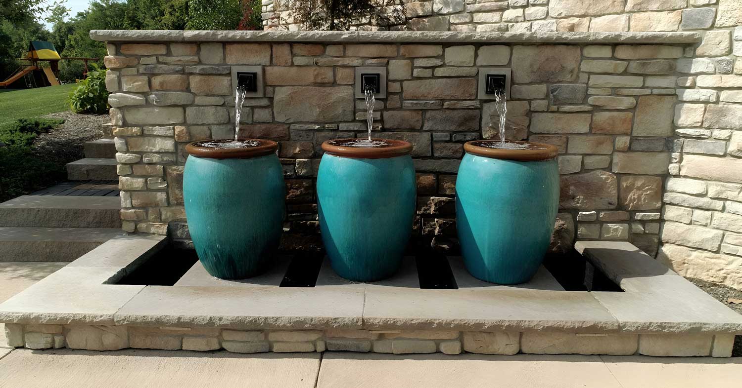 foskett-stiles-water-feature Large ceramic vases in a rich turquoise hue bring dynamic contrast to this modern water feature against a backdrop of rugged stone retaining wall.