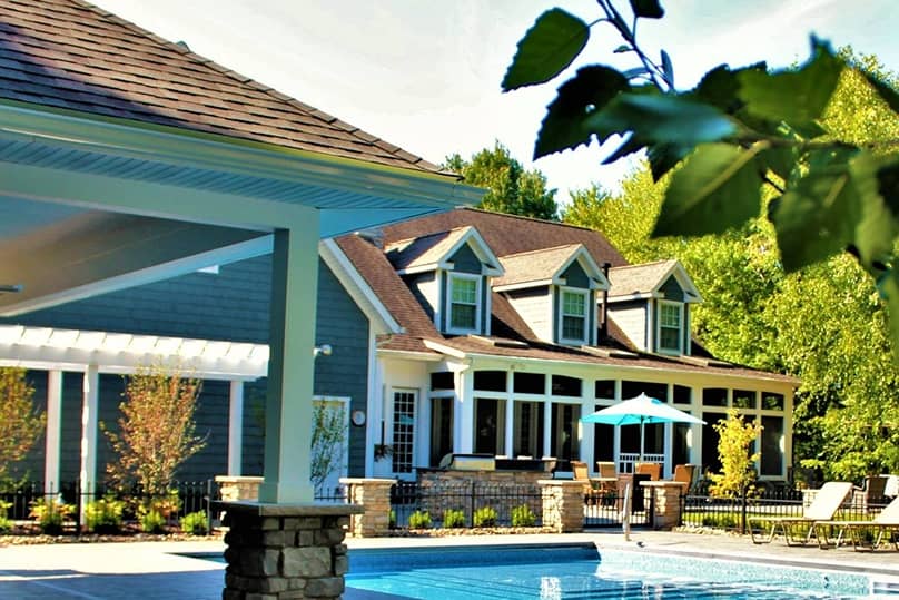 pool-through-leaves the back of a home with a four seasons room next to a pool on a sunny day